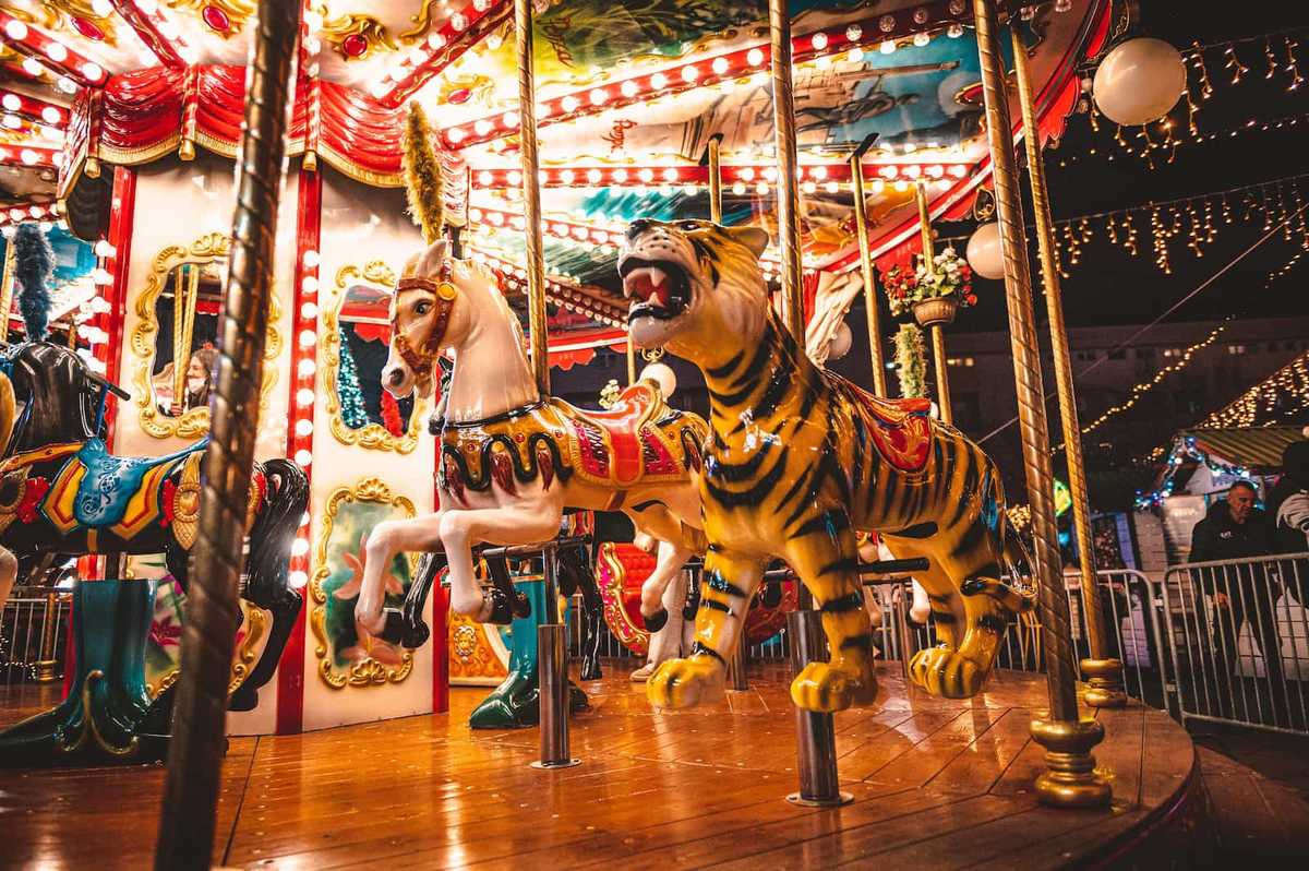 A carousel at night with bright lights. Figures of a horse and tiger are visible.