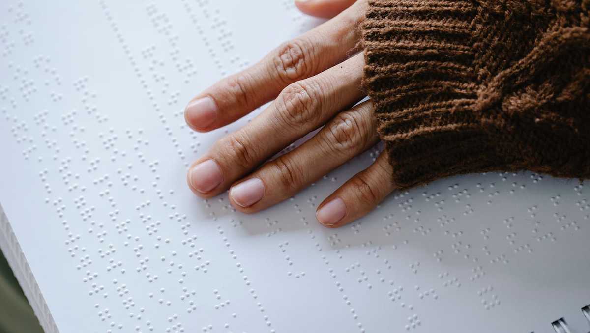 Fingers touch the page of a book in Braille.