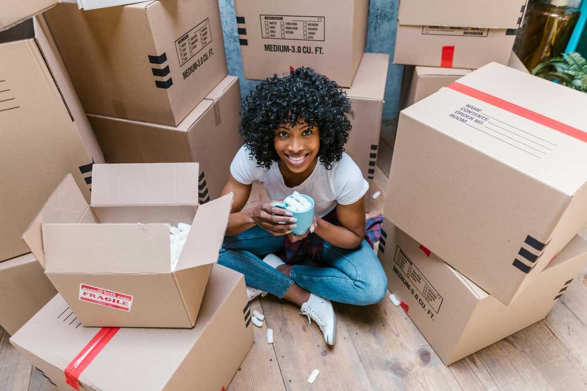 A woman sitting on the floor surrounded by cardboard boxes.